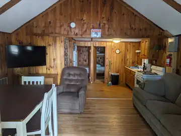 Interior living area of The Cottage featuring rustic pine paneling, flat-screen TV, and full kitchen